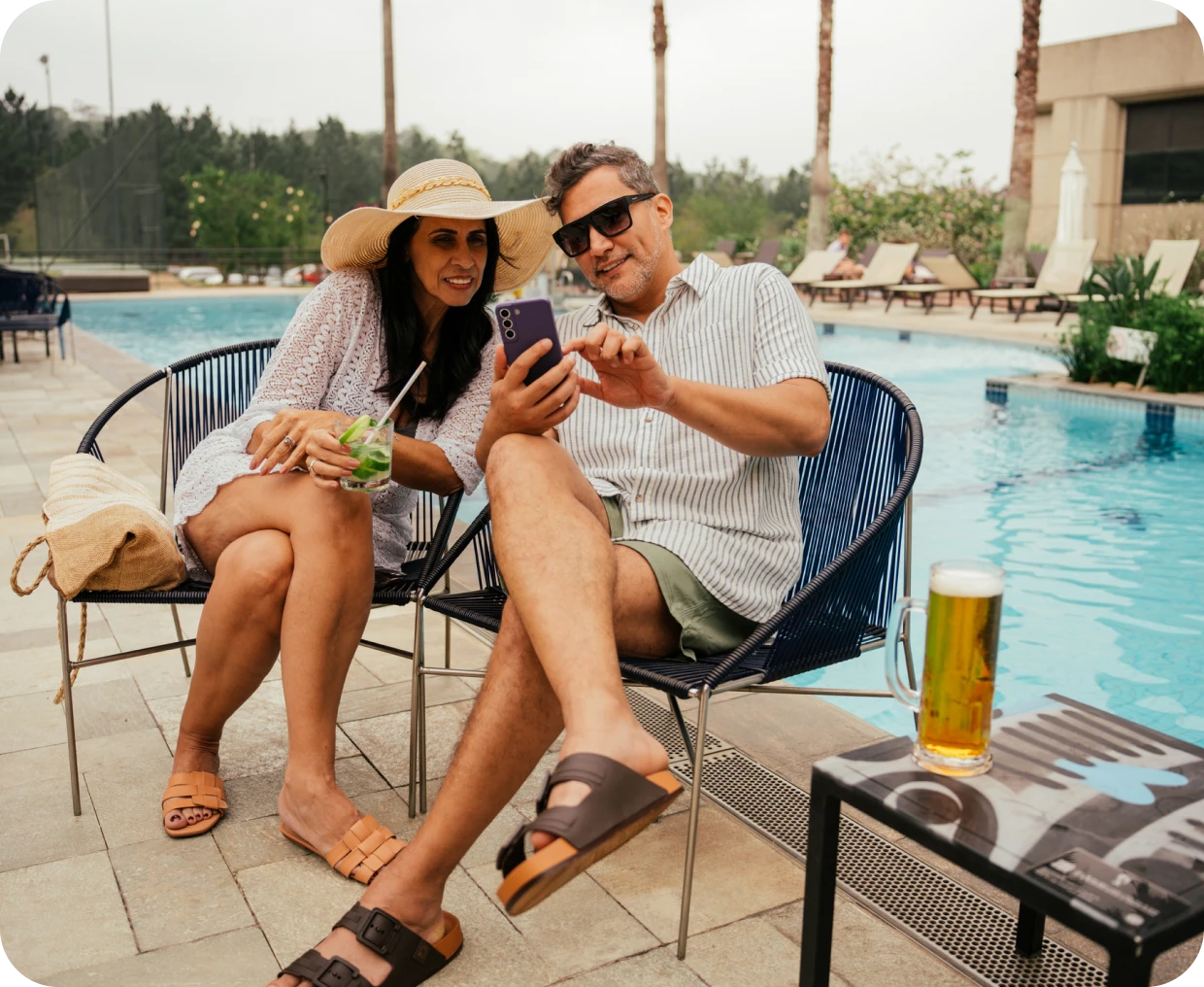 Couple relaxing poolside with drinks and phone.