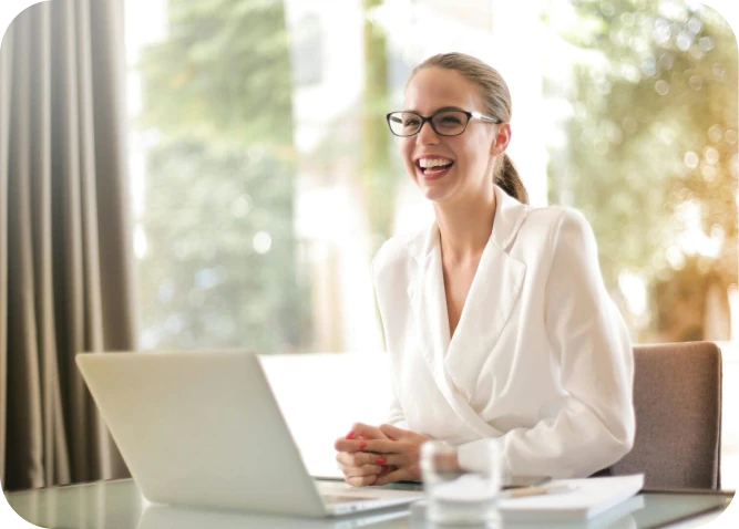 Smiling woman in white blazer, using laptop.